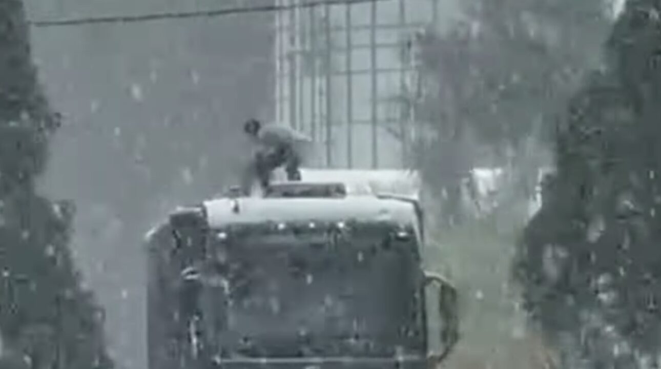 Caminhoneiro cobre carga embaixo de chuva enquanto colegas filmam sem ajudar