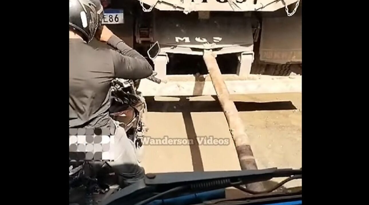 Motociclista se posiciona entre caminhão sendo puxado por cabão