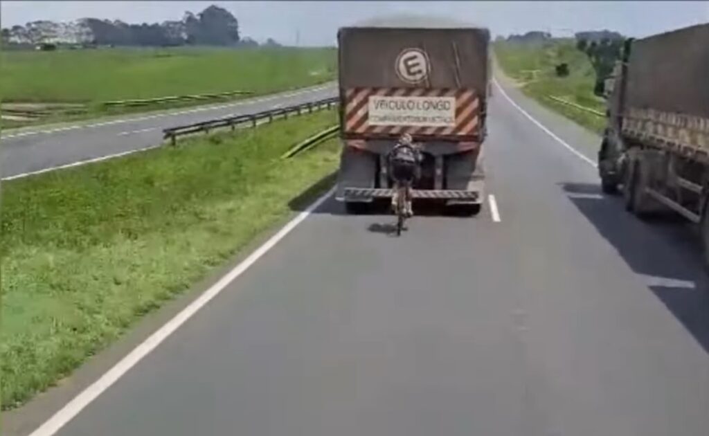 Ciclista se aproxima perigosamente da traseira de carreta em rodovia movimentada