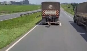 Ciclista se aproxima perigosamente da traseira de carreta em rodovia movimentada