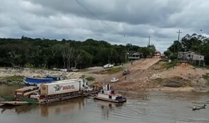 Carretas carregadas enfrentam dificuldades ao sair da balsa no Rio Igapó-Açu