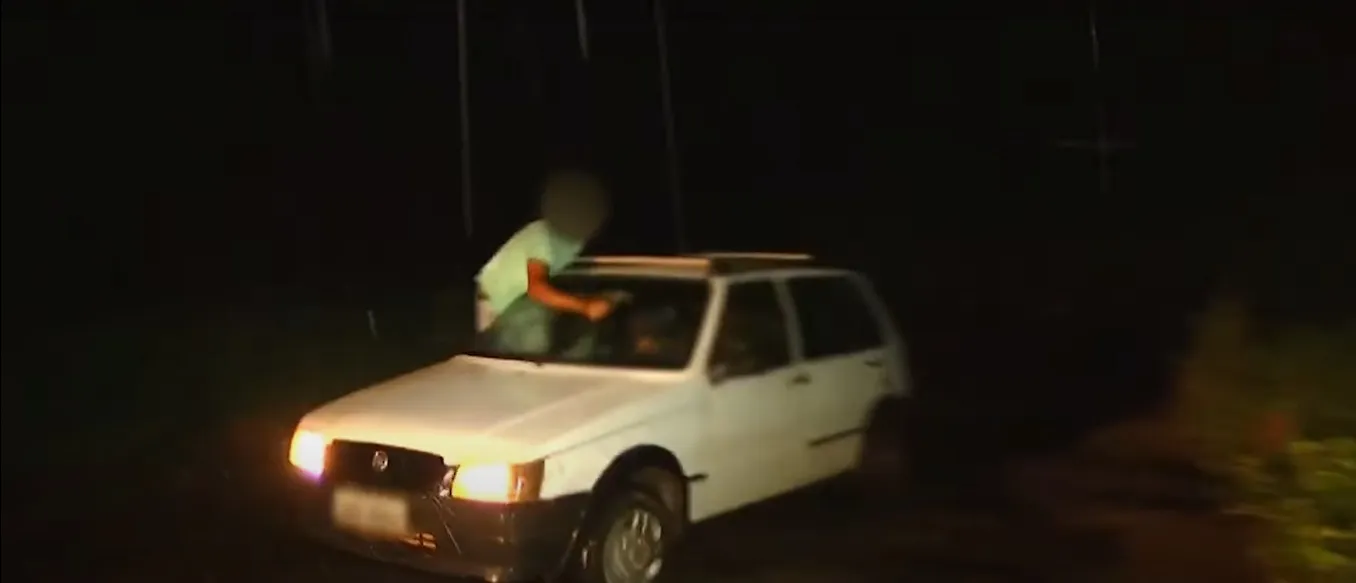 Homem dirige veículo com carona movimentando limpador de para-brisa manualmente