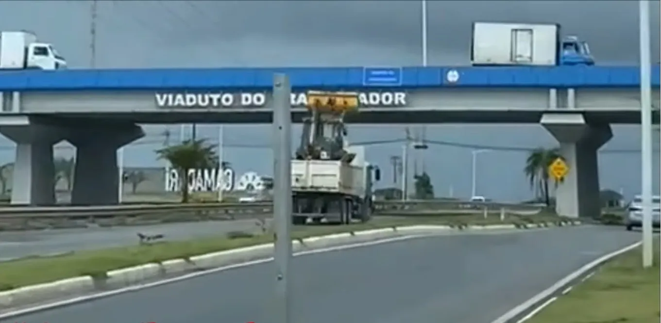 Caminhão carregado com máquina com concha levantada quase provoca tragédia